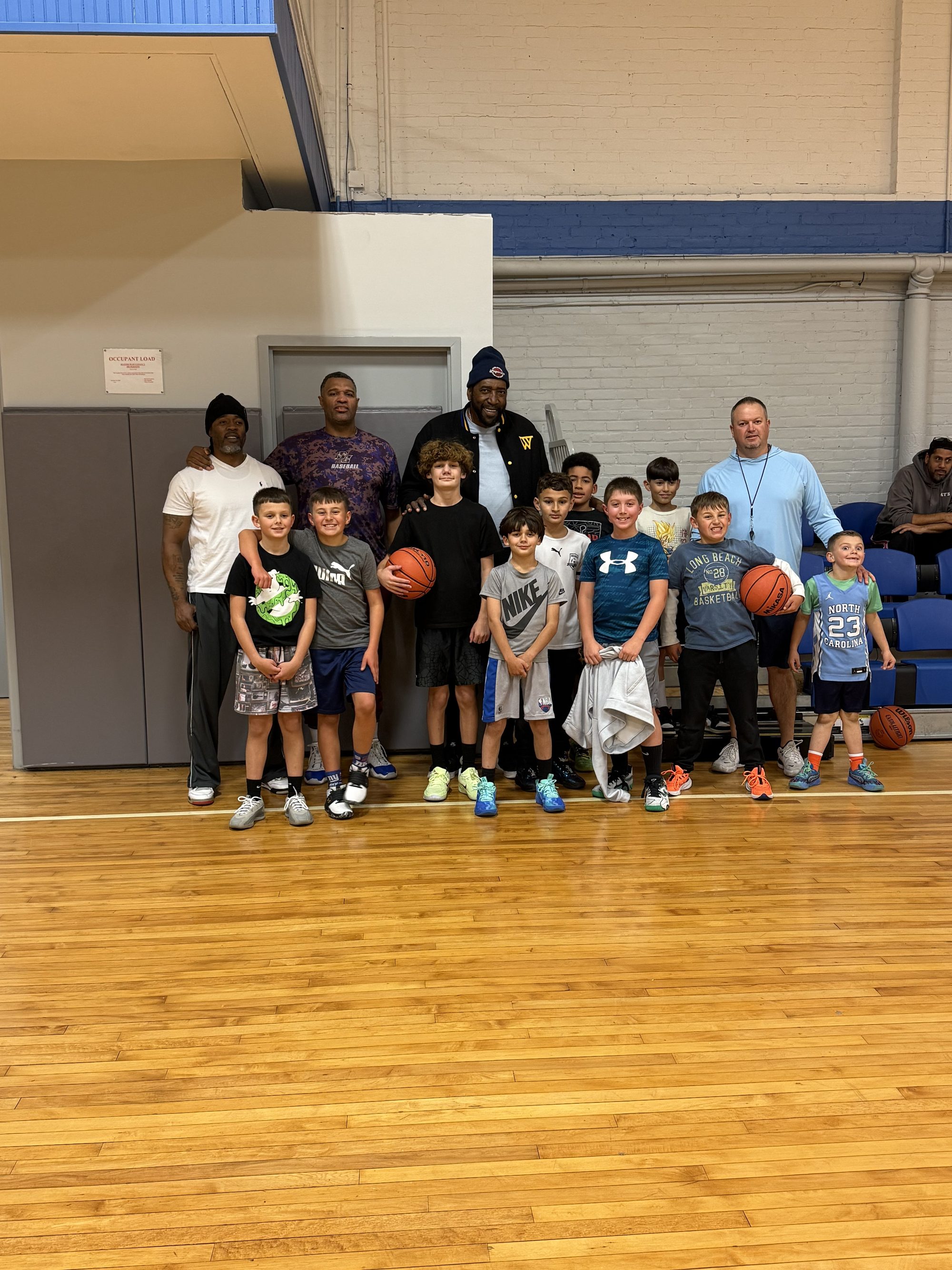 Coach Clifford Ray with a group of kids and their basketballs in a school gym