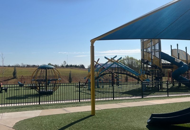 A shaded school playground with climbing structures and a slide